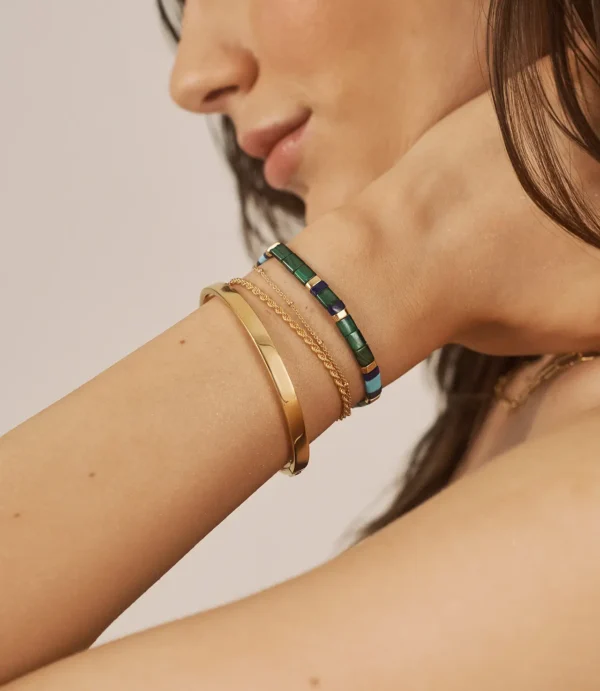 Close-up wrist with gold and green bracelets