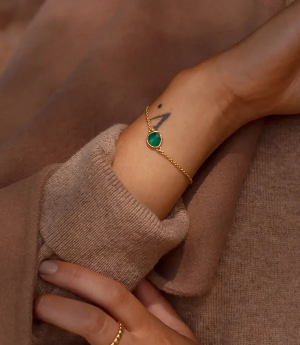 Wrist wearing gold bracelet with green gemstone